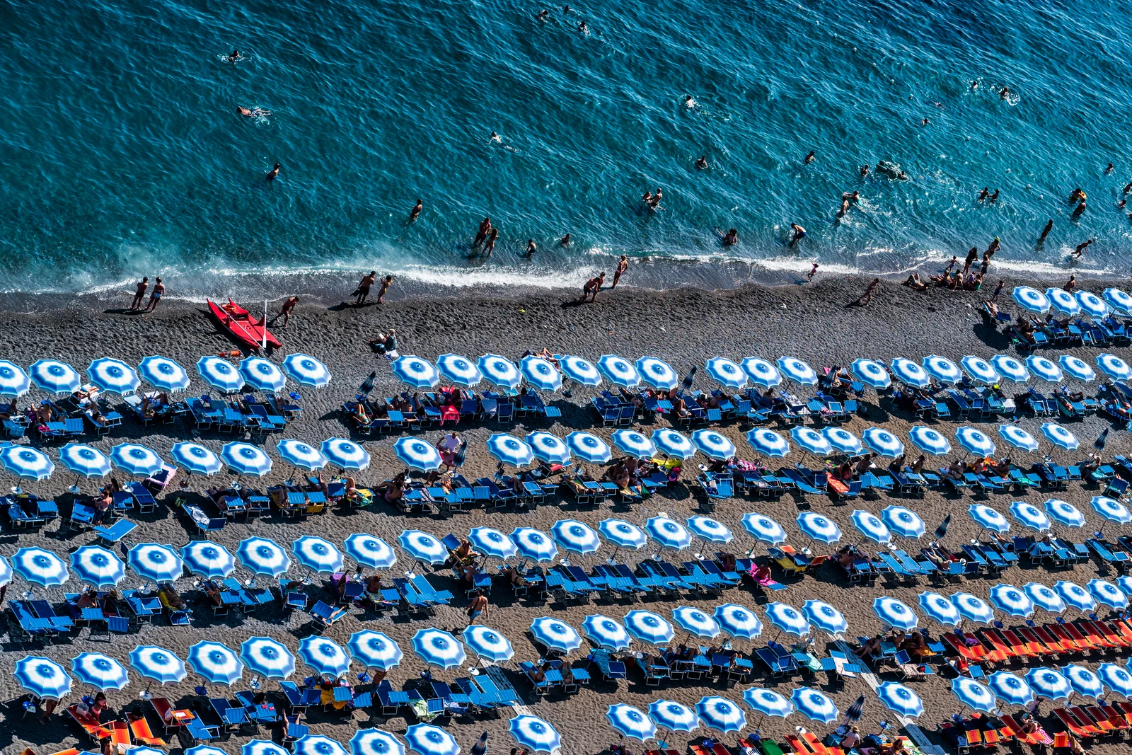 Crowded Spiaggia Grande beach in Positano with rows of umbrellas and boats in the bay