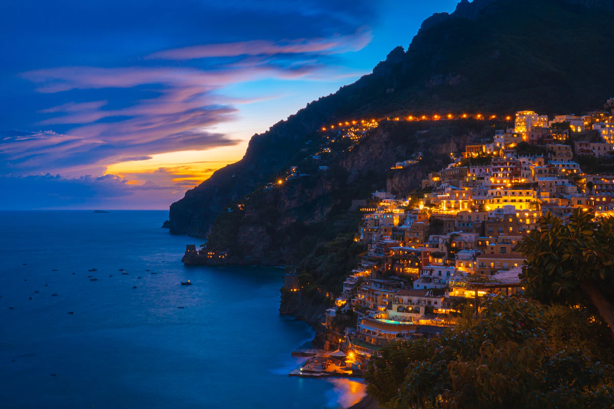 Positano lit up at twilight with buildings glowing against the cliff